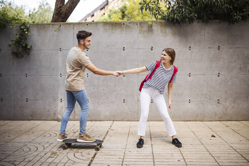 Freund hält die Hand seiner Freundin beim Skateboardfahren auf dem Gehweg - GRCF00721