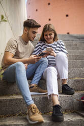 Paar benutzt Mobiltelefon, während es auf einer Treppe sitzt - GRCF00733