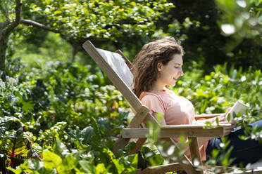 Frau liest ein Buch und sitzt auf einem Stuhl im Garten - SBOF03790