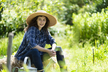 Lächelnde Frau schaut weg, während sie im Garten auf Heu sitzt - SBOF03796