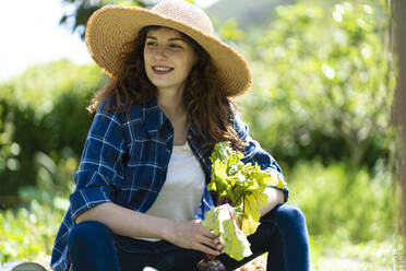 Woman with sunhat holding beetroot plant in garden - SBOF03797