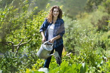 Woman holding watering can while standing in garden - SBOF03804