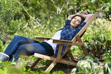 Young woman sleeping on chair in organic vegetable garden - SBOF03813