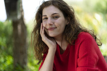 Smiling woman with hand on chin in garden - SBOF03841