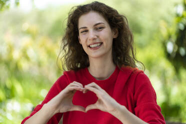 Smiling young woman making heart shape with hands - SBOF03844