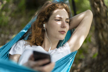 Nachdenkliche Frau hört Musik und entspannt sich in der Hängematte - SBOF03846