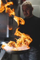 Koch hält flammende Pfanne in der Küche - JAQF00653