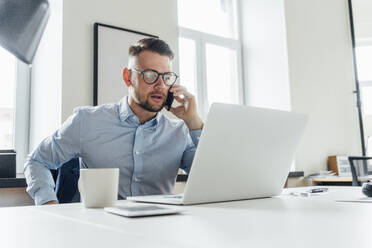 Mittlerer erwachsener Geschäftsmann, der im Büro mit einem Mobiltelefon spricht - VPIF04058