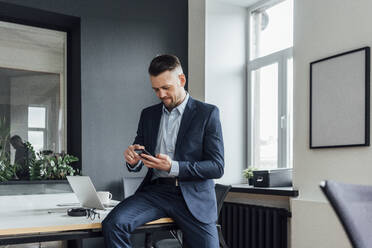 Mittlerer Erwachsener, männlicher Berufstätiger, der am Schreibtisch sitzend ein Mobiltelefon benutzt - VPIF04070