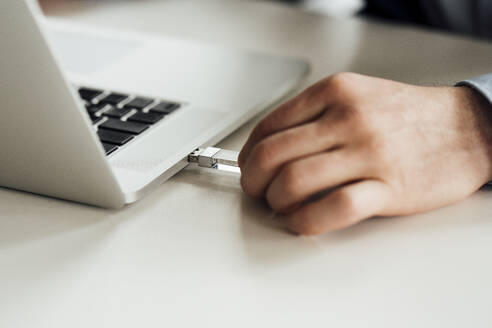 Geschäftsmann, der ein Laufwerk in einen Laptop auf dem Schreibtisch steckt - VPIF04077