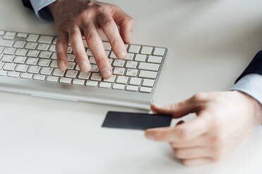 Businessman holding card while typing on computer keyboard in office - VPIF04080