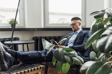 Männlicher Unternehmer, der im Büro sitzend ein Smartphone benutzt - VPIF04088