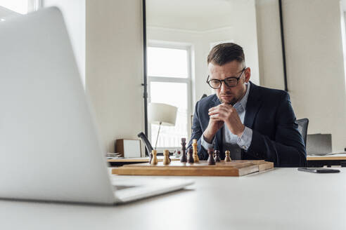 Männlicher Unternehmer mit Hand am Kinn spielt Schach im Büro - VPIF04094