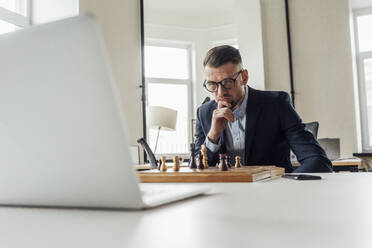 Geschäftsmann schaut auf Laptop beim Schachspielen im Büro - VPIF04095