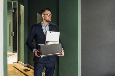 Male entrepreneur holding box while standing in office - VPIF04097