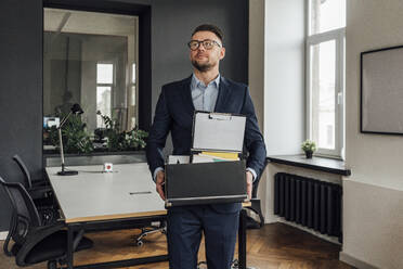 Businessman holding belongings in cardboard box at office - VPIF04098