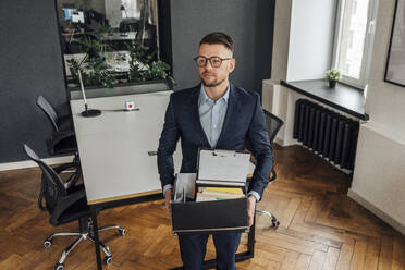 Thoughtful male entrepreneur holding belongings while standing at office - VPIF04099