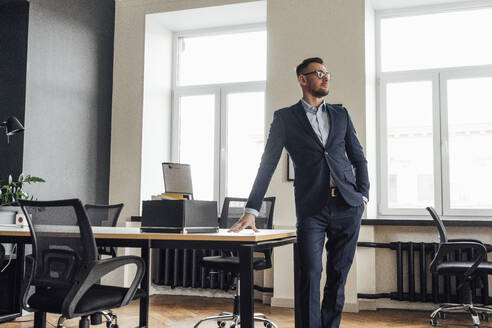 Mid adult male entrepreneur standing with hands in pockets at place of work - VPIF04100