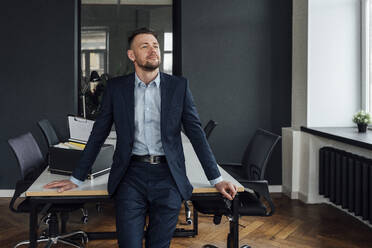 Thoughtful businessman leaning on desk with office supply box - VPIF04101