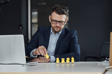 Männlicher Unternehmer mit Laptop, der ein Baby-Huhn-Spielzeug im Büro hält - VPIF04105