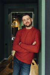 Smiling male professional standing with arms crossed leaning on wall at office - VPIF04124