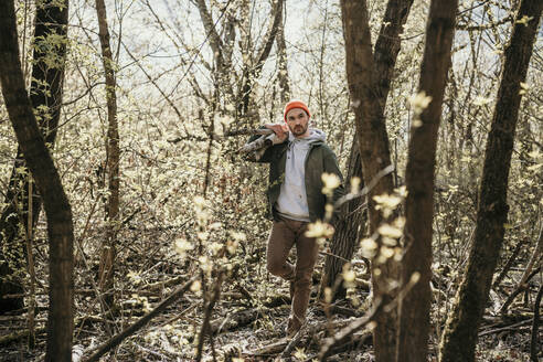 Mann trägt Holz auf der Schulter inmitten kahler Bäume im Wald - MJRF00584