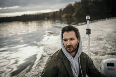 Handsome man wearing hood while traveling in boat on lake - MJRF00590