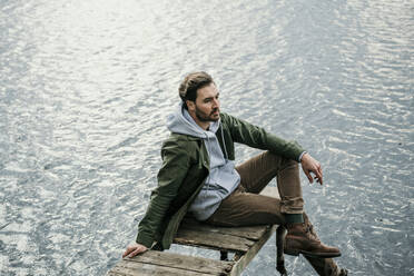 Nachdenklicher Mann, der auf dem Steg über dem Seddinsee sitzt und wegschaut - MJRF00601