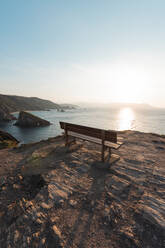 Empty bench standing at edge of coastal cliff at sunset - RSGF00696