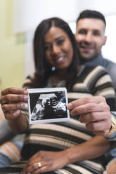 Wife with husband holding ultrasound scan results - JAQF00656