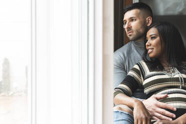 Mid adult couple looking away through window at home - JAQF00658