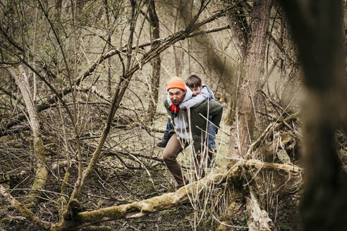 Vater nimmt Sohn huckepack durch kahle Bäume im Wald - MJRF00611