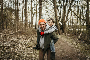 Lachender Vater, der seinen Sohn im Wald huckepack nimmt - MJRF00614