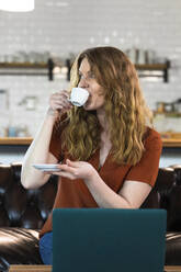 Businesswoman looking away while drinking coffee in office cafeteria - FKF04170