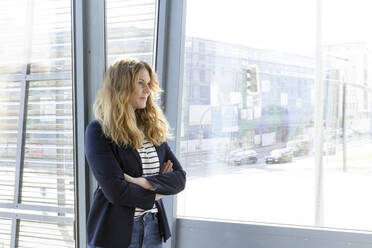 Businesswoman with arms crossed contemplating while standing by window in office - FKF04195