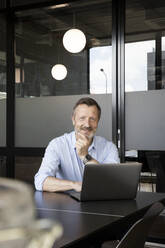 Male professional smiling while sitting in front of laptop at office - FKF04204