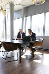 Businessmen discussing business plan while sitting at desk in office - FKF04230