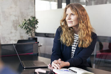 Geschäftsfrau mit braunen Haaren, die beim Sitzen im Büro wegschaut - FKF04252