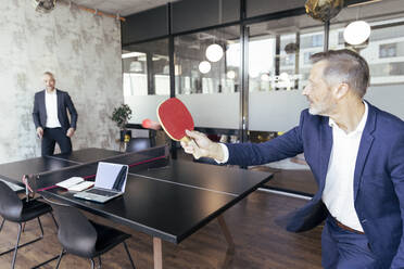 Male professionals playing table tennis at office - FKF04257