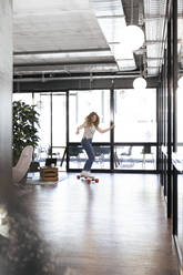 Businesswoman riding skateboard in office - FKF04283