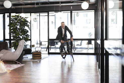 Lächelnder Geschäftsmann beim Radfahren im Büro - FKF04285