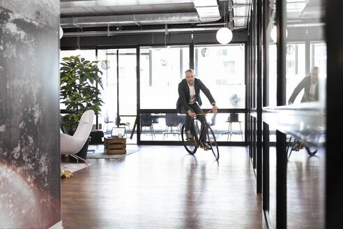 Männlicher Unternehmer fährt Fahrrad im Büro - FKF04286