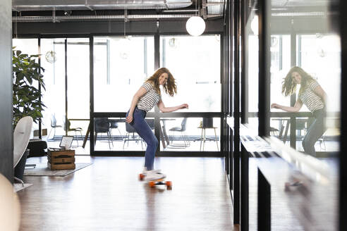 Lächelnde kreative Geschäftsfrau auf dem Skateboard im Büro - FKF04291