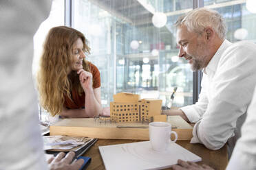 Lächelnde Architektin und lächelnder Architekt betrachten ein Modell im Büro - FKF04306