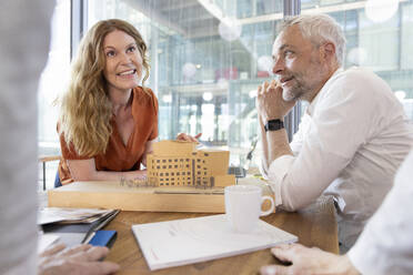 Lächelnde Architektin und lächelnder Architekt diskutieren am Schreibtisch im Büro - FKF04307