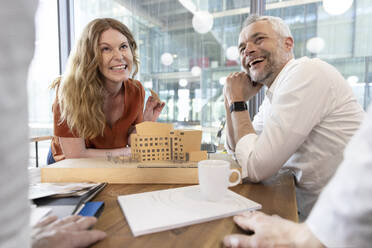 Lächelnde männliche und weibliche Architekten, die einen Kollegen ansehen, während sie am Schreibtisch im Büro diskutieren - FKF04308