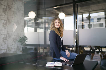 Businesswoman day dreaming while sitting on table at office - FKF04326