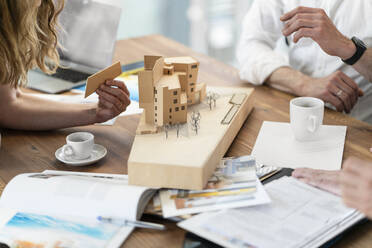 Architektin arrangiert Architekturmodell mit männlichen Kollegen am Schreibtisch im Büro - FKF04335