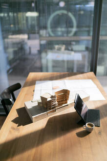 Sonnenlicht fällt auf ein architektonisches Modell und eine Blaupause auf einem Tisch im Büro - FKF04343