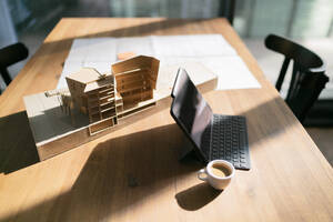 Laptop mit Kaffeetasse und Architekturmodell auf einem Tisch im Büro - FKF04346
